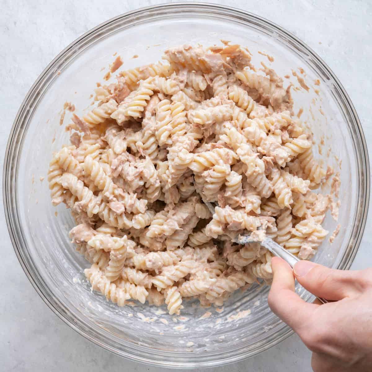 Tossing pasta with tuna and dressing.