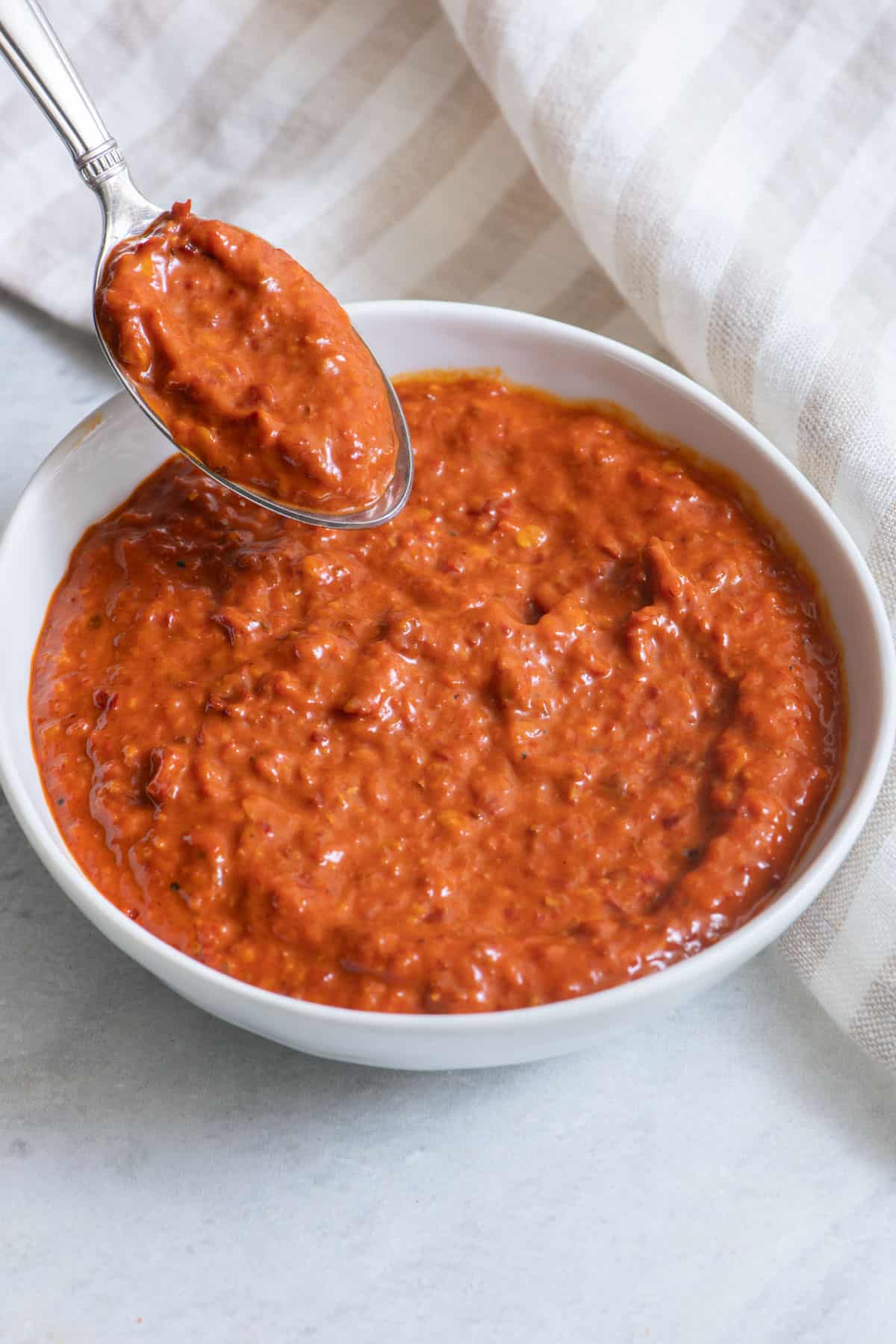 White bowl filled with harissa and a spoon overtop with some on it.