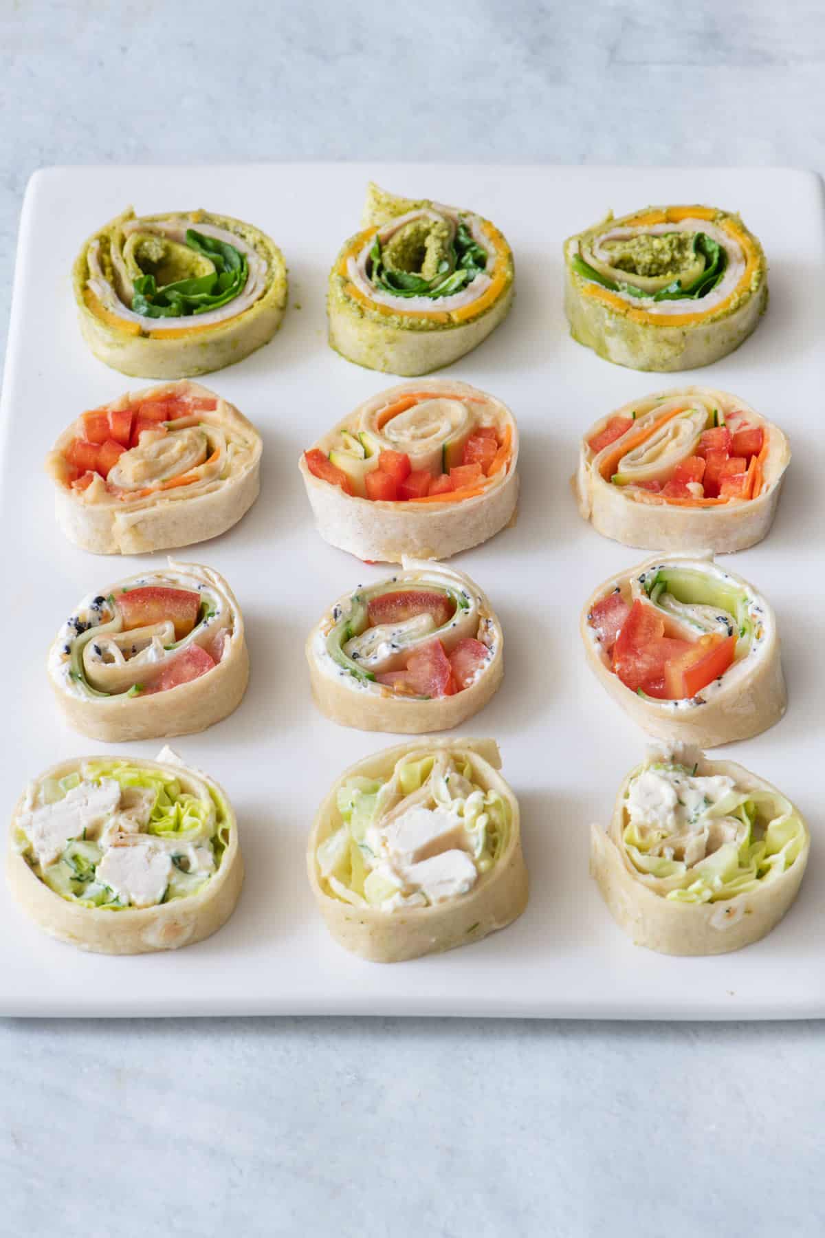 Rectangle dish with 4 different style pinwheel sandwiches, 3 of each kind, in rows.