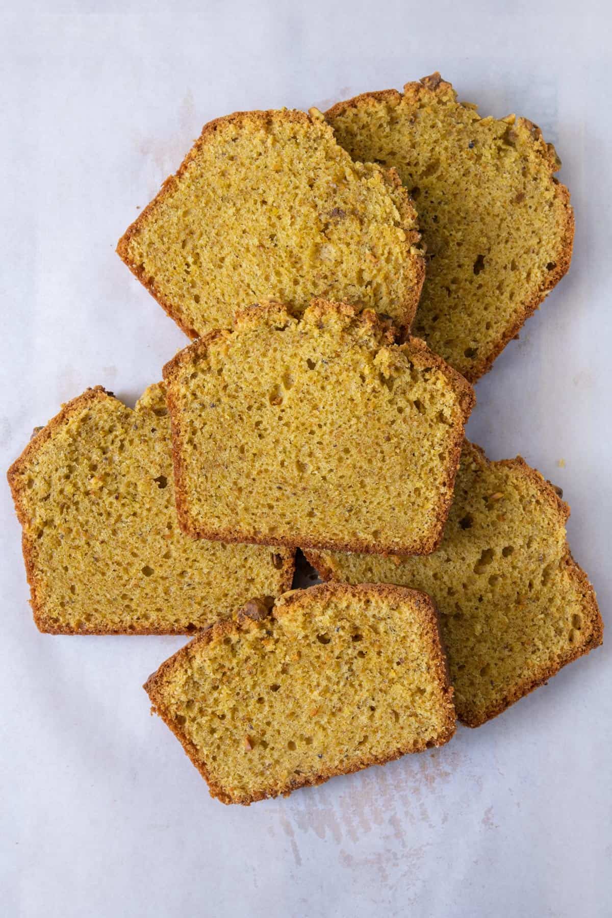 Overhead view of 6 thick slices of pistachio sweet bread stacked over each other on parchment paper.