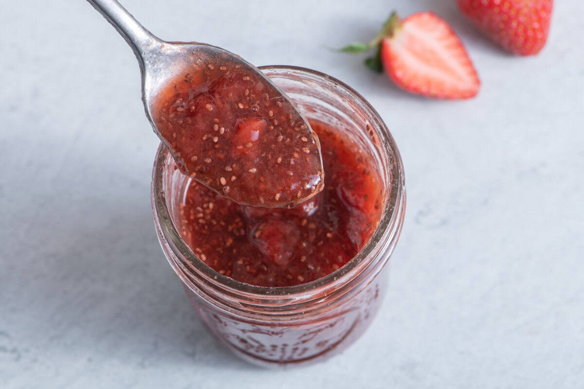 Strawberry chia jam in a jar with a spoon holding up some and strawberries nearby.