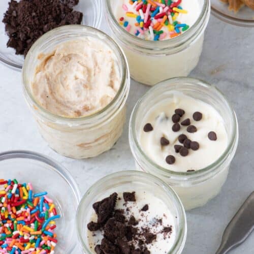 Jars of ice cream with toppings on each and jars of more toppings nearby.