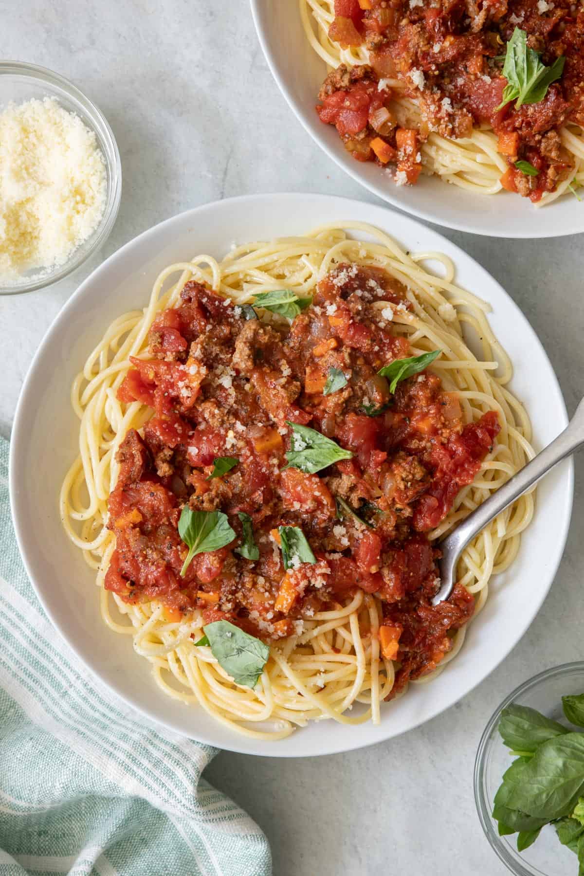 Shallow bowl of cooked spaghetti with chunky red sauce added on top and another bowl off to the side.
