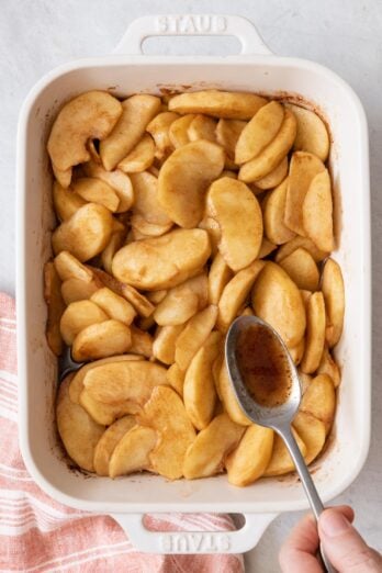 Slices of apples after being baked and a spoon pouring the spiced butter sauce over them.