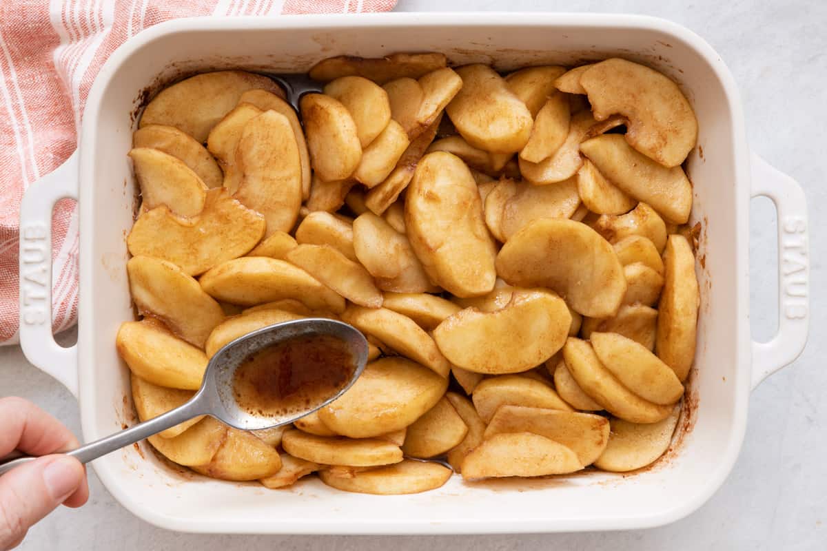 Slices of apples after being baked and a spoon pouring the spiced butter sauce over them.