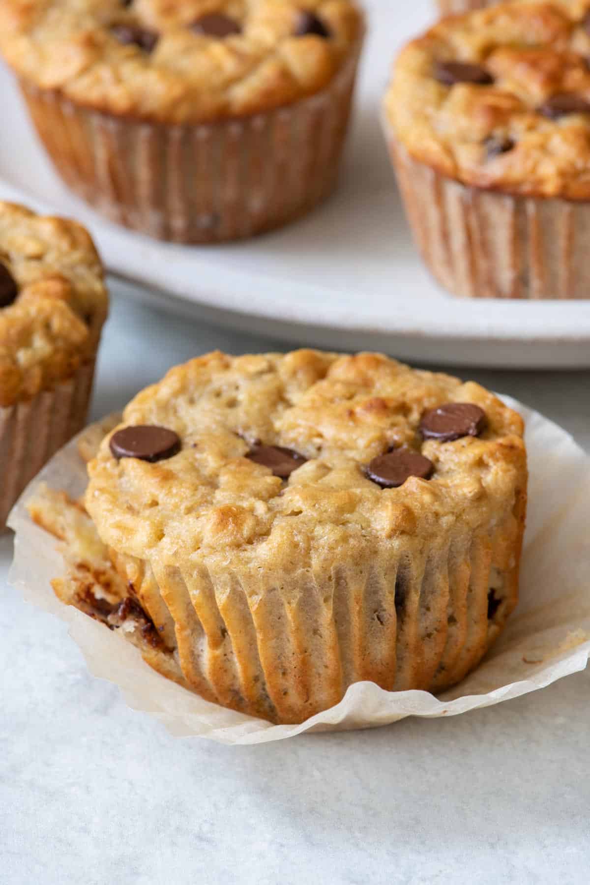 Close up of single muffin with liner peeled and other muffins around.
