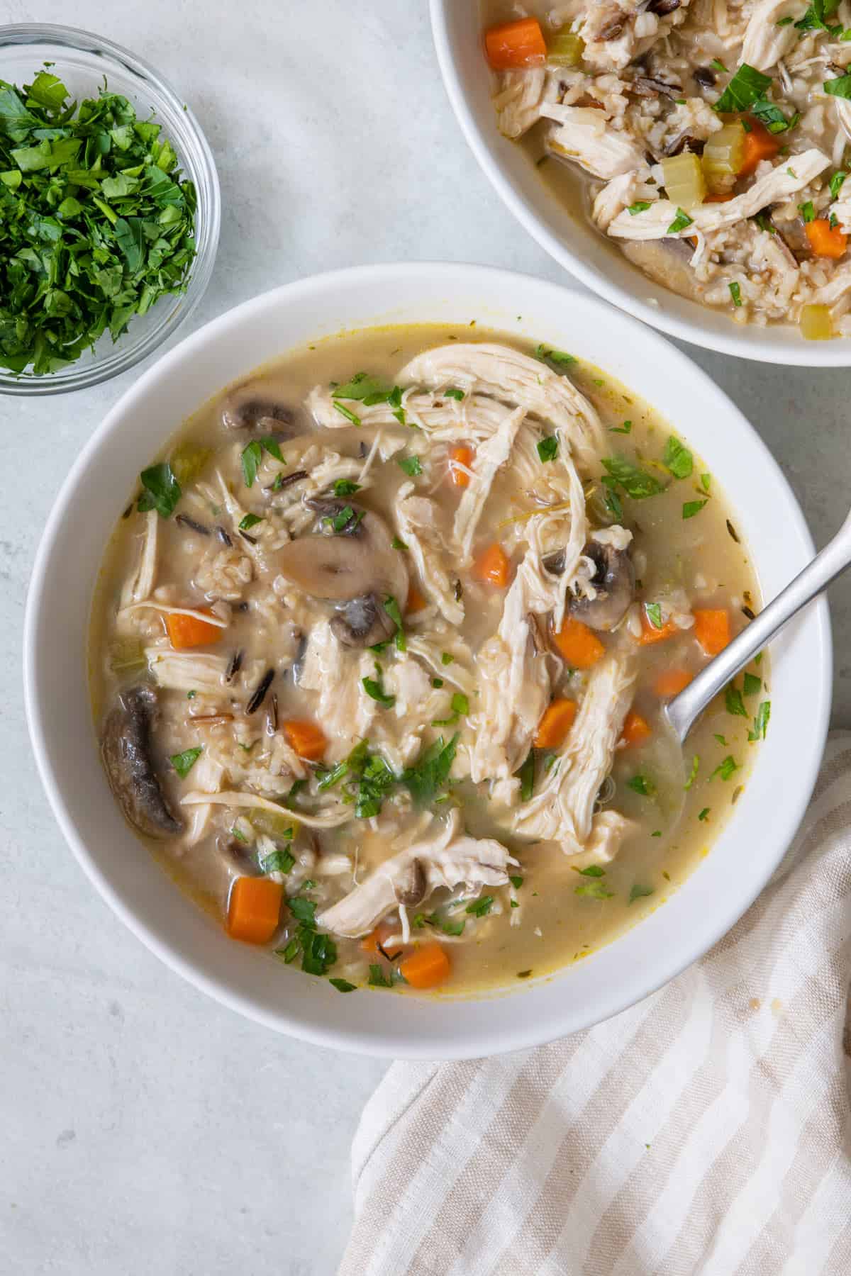 Closed in shot of a bowl of chicken mushroom soup with a soup soon dipped inside.