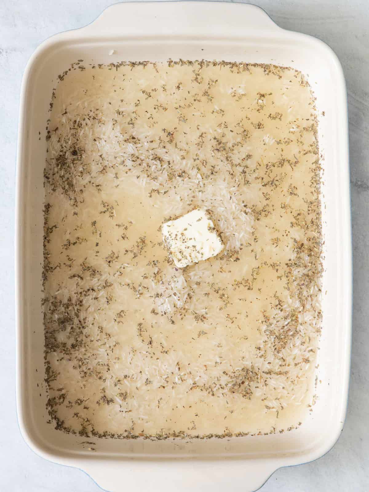 Uncooked rice, stock and seasoning in baking dish.