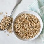 Small bowl of roasted sunflower seeds with spoon next to bowl overflowing with seeds.