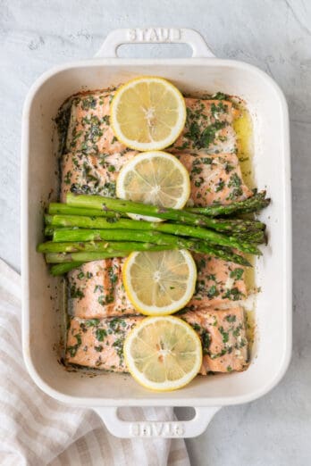 Roasted salmon and asparagus in baking dish garnished with thin lemon slices.