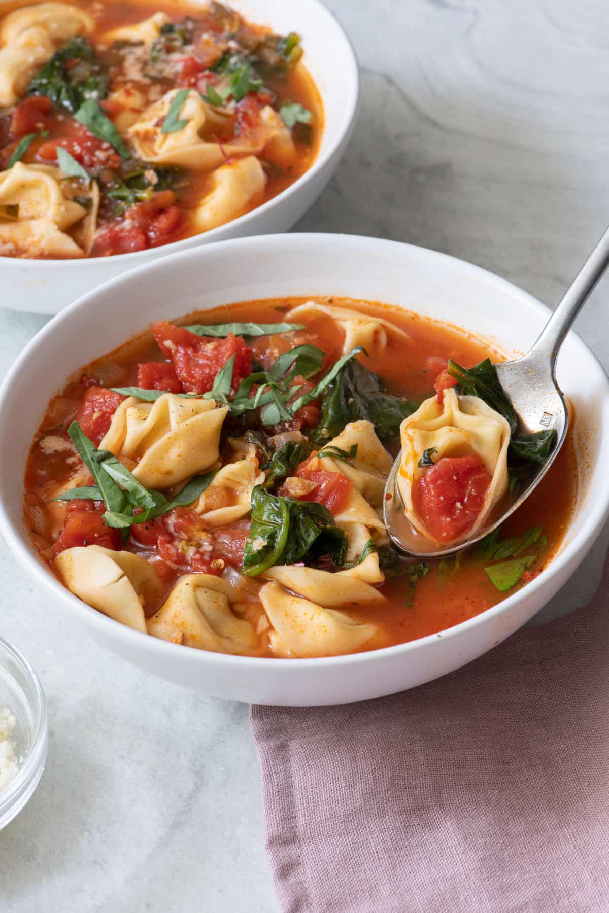 Angled side view of a white bowl filled with soup and a spoon picking up some.