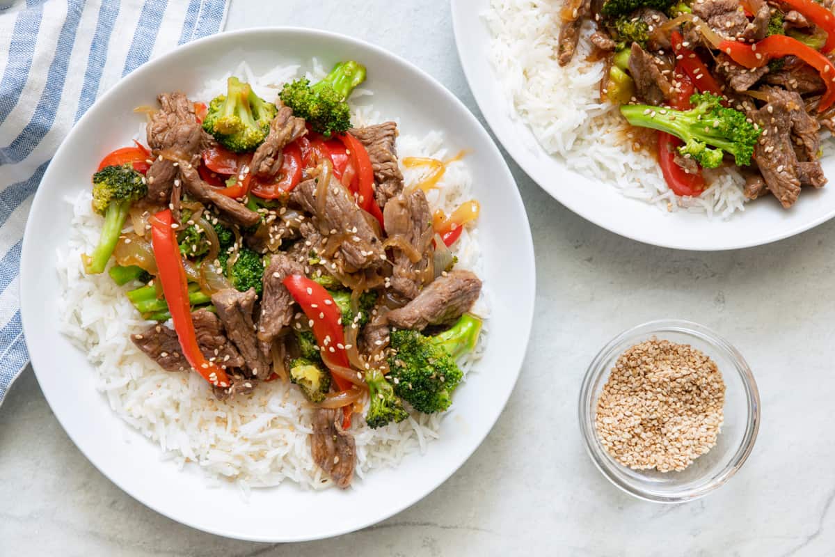 Two plates of recipe with one off to side served over recipe and garnished with sesame seeds.