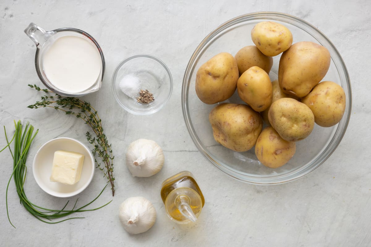 Ingredients for recipe: cream, fresh herbs, butter, seasoning, 2 whole garlic heads, and potatoes.