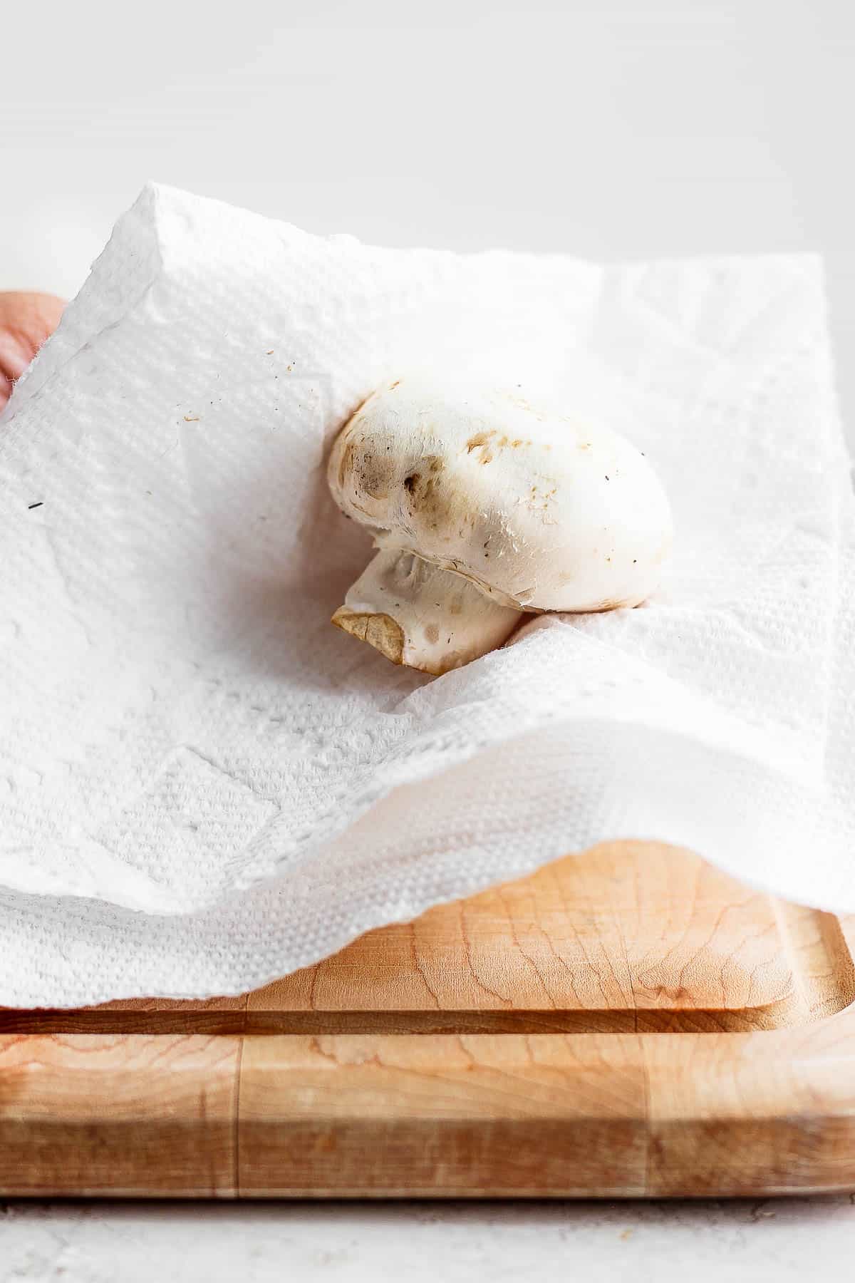Cleaning a whole mushroom with damp paper towel.