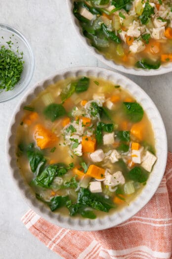 A bowl of leftover turkey and rice soup with another bowl nearby.