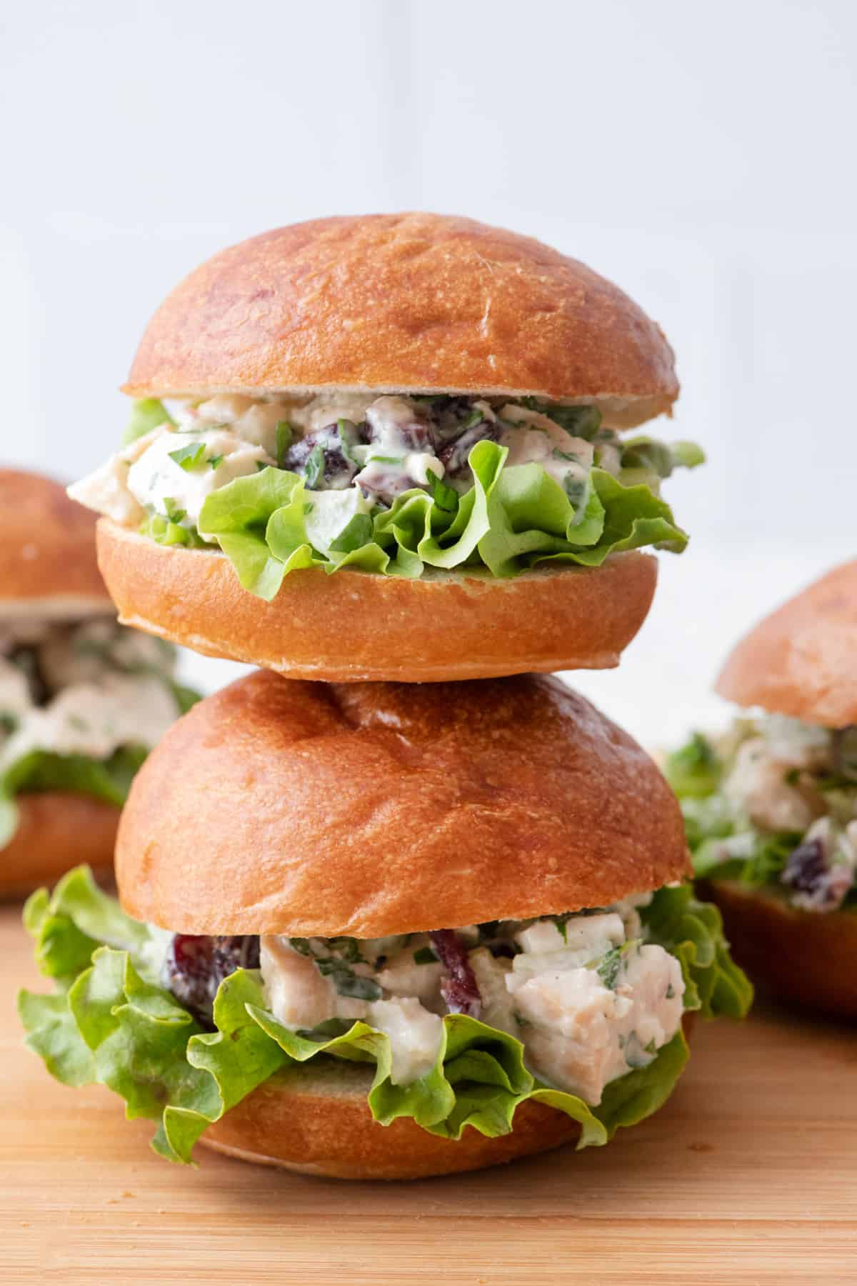 A few turkey salad sandwichs served on dinner rolls with leafy lettuce stacked on top of eachother on a cutting board.