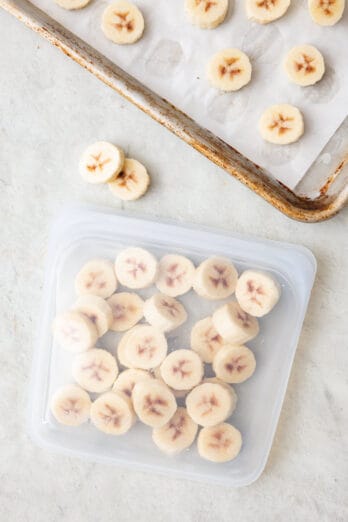 Frozen banana slices inside a reusable freezer bag with tray of them nearby.