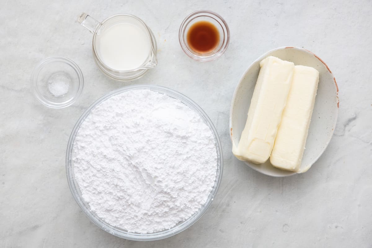 Ingredients for recipe in individual bowls, salt, milk, confectioner's sugar, vanilla, and 2 sticks of butter.