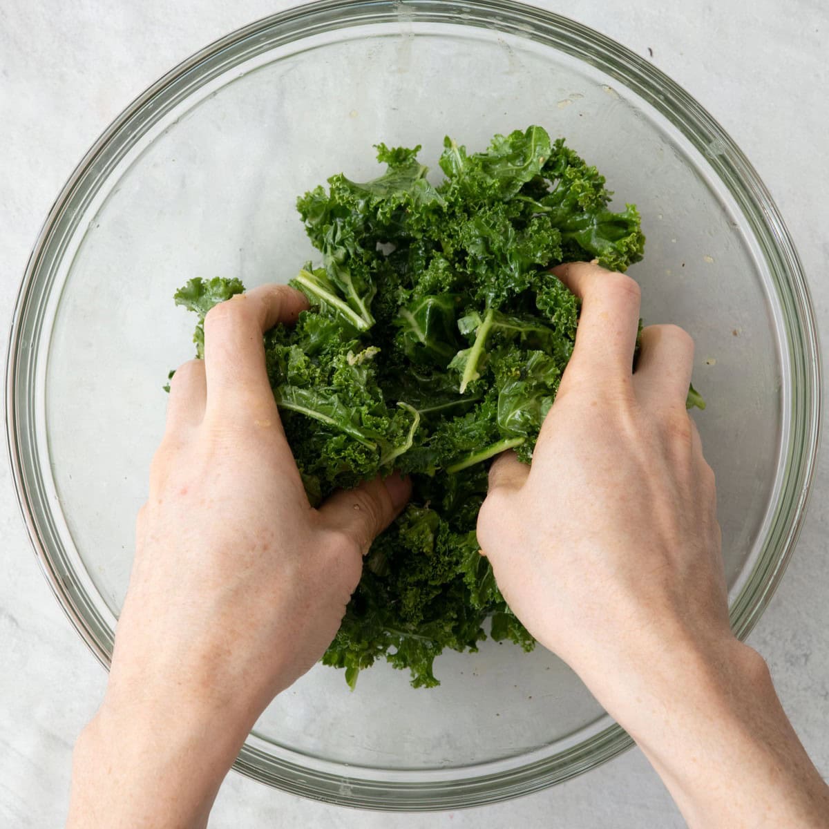 Hands in bowl massaging dressing into kale.