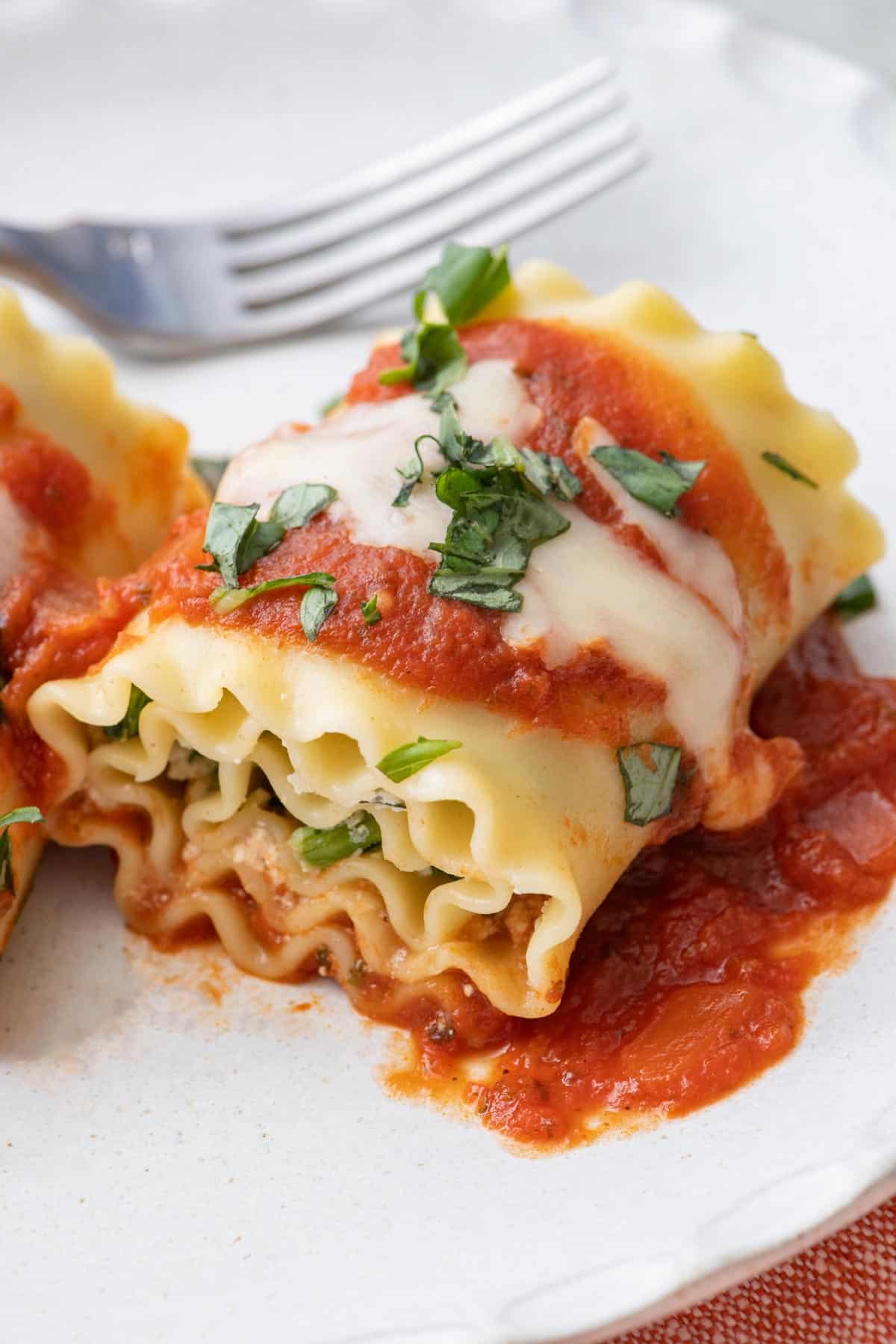 Close up of lasagna roll up garnished with fresh chopped basil on a small plate with fork.