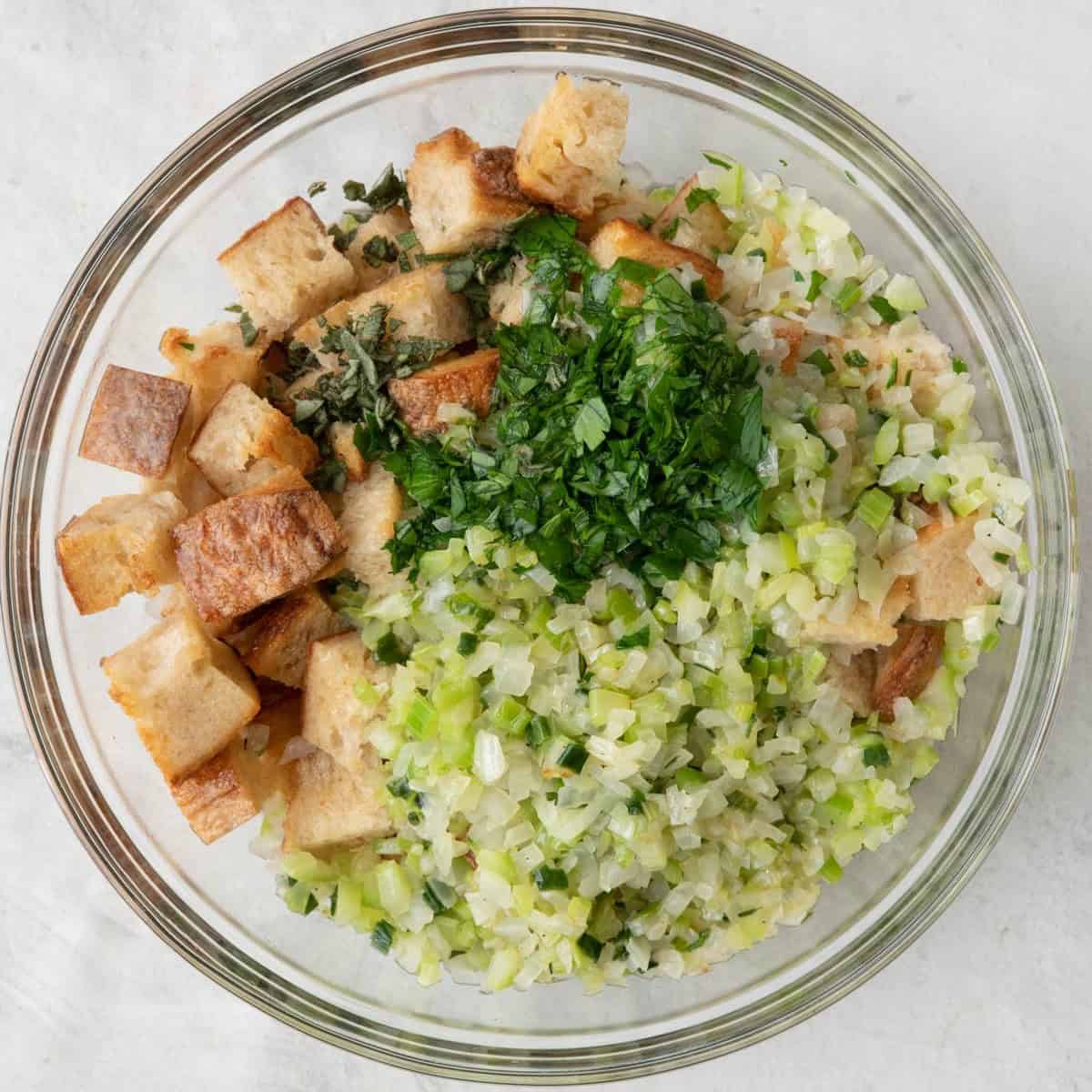 Bowl with toasted bread cubes, cooked vegetables, herbs, chicken stock added.