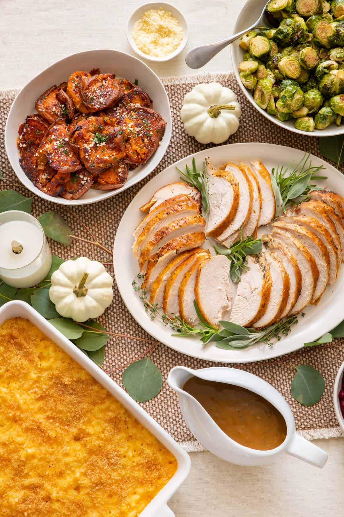 Thanksgiving table serving sliced turkey breast, smashed sweet potatoes, roasted brussel sprouts, baked mac and cheese, and gravy.