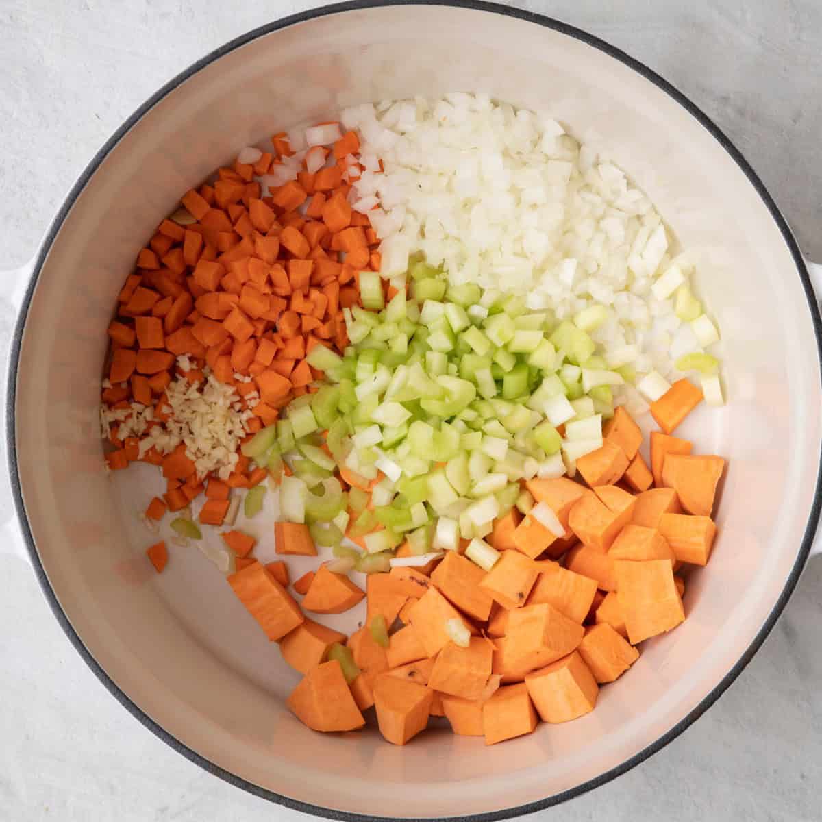 Onions, carrots, celery, garlic, and sweet potato cubes in pot.