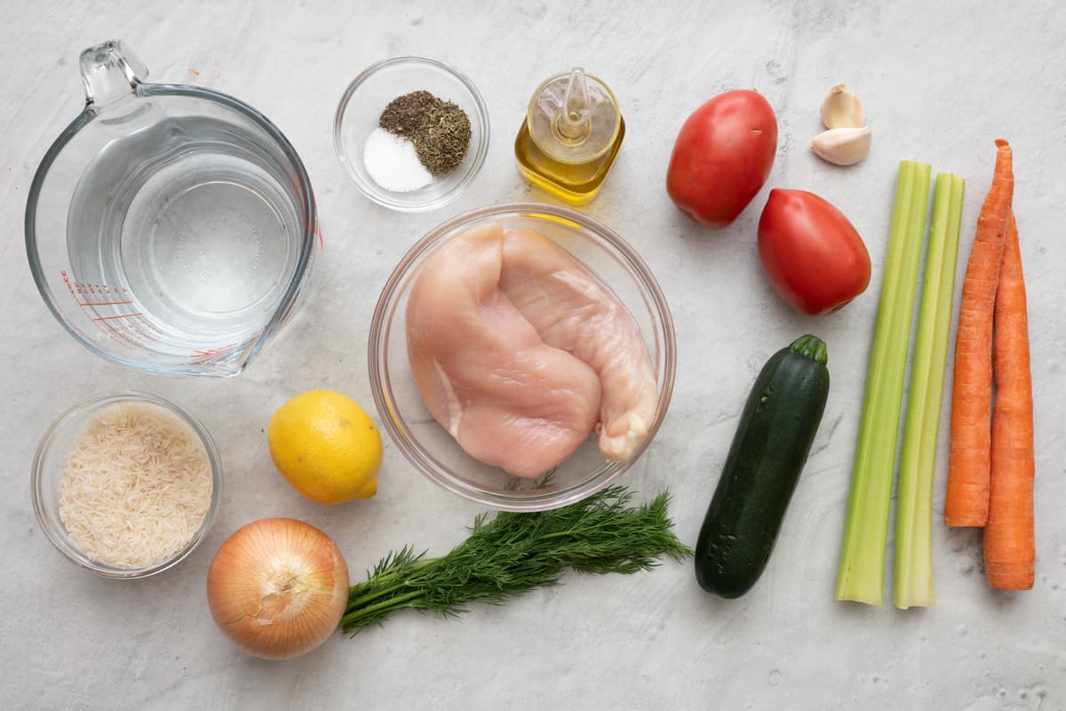 Ingredients for recipe before being prepped: water, rice, onion, lemon fresh dill, chicken breast, seasoning, oil, tomatoes, zucchini, garlic, celery, and carrots.