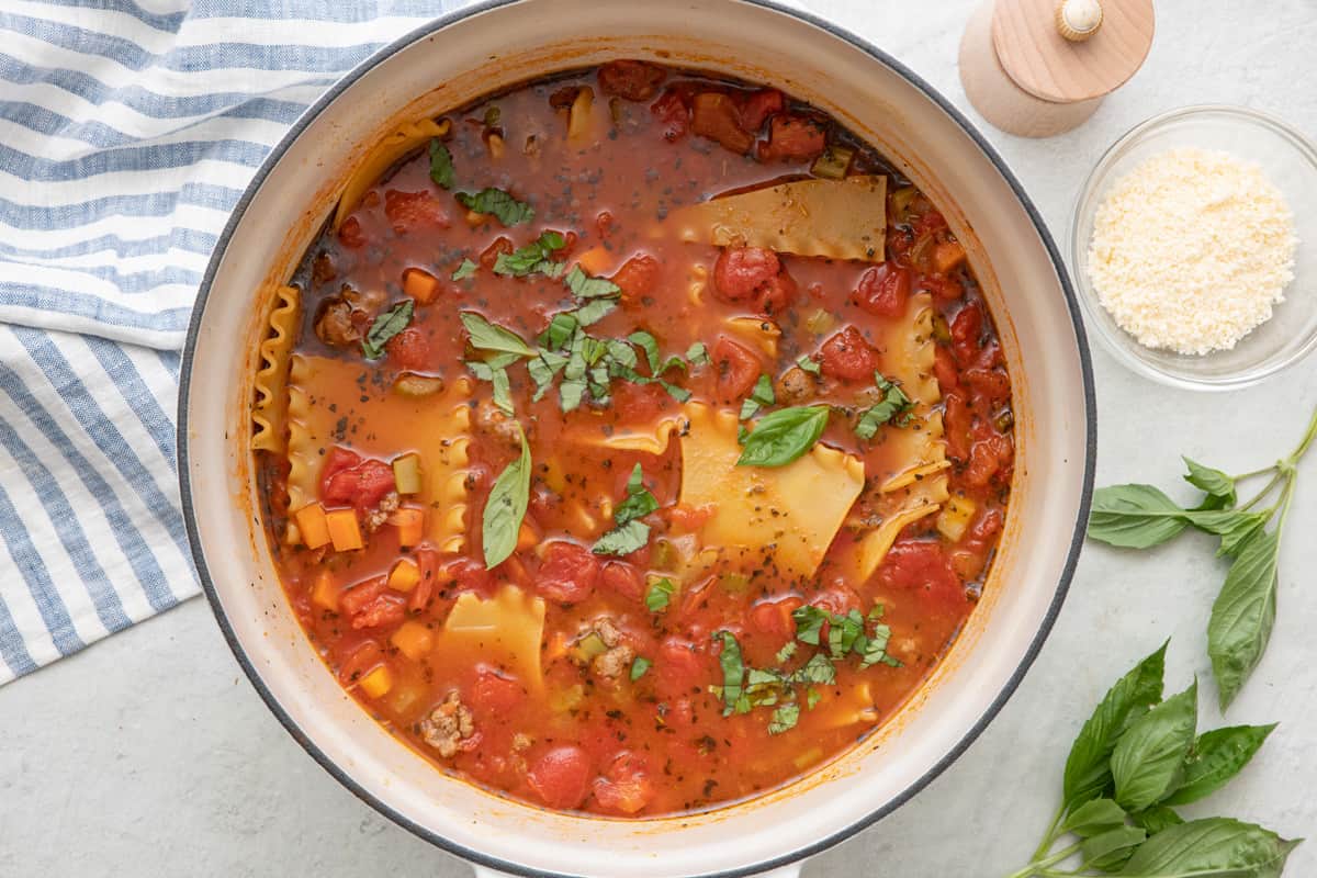 Overhead shot of lasagna soup garnished with fresh basil with a bowl of grated parmesan nearby.