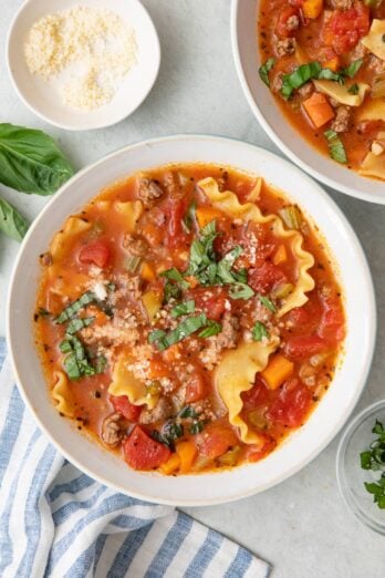 Bowl of lasagna soup garnished with torn basil and parmesan cheese with another bowl nearby.