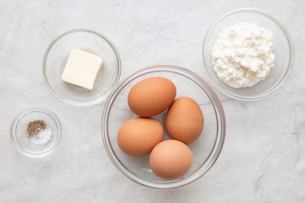 Ingredients for recipe in individual bowls: salt and pepper, butter, 4 whole eggs, and cottage cheese.