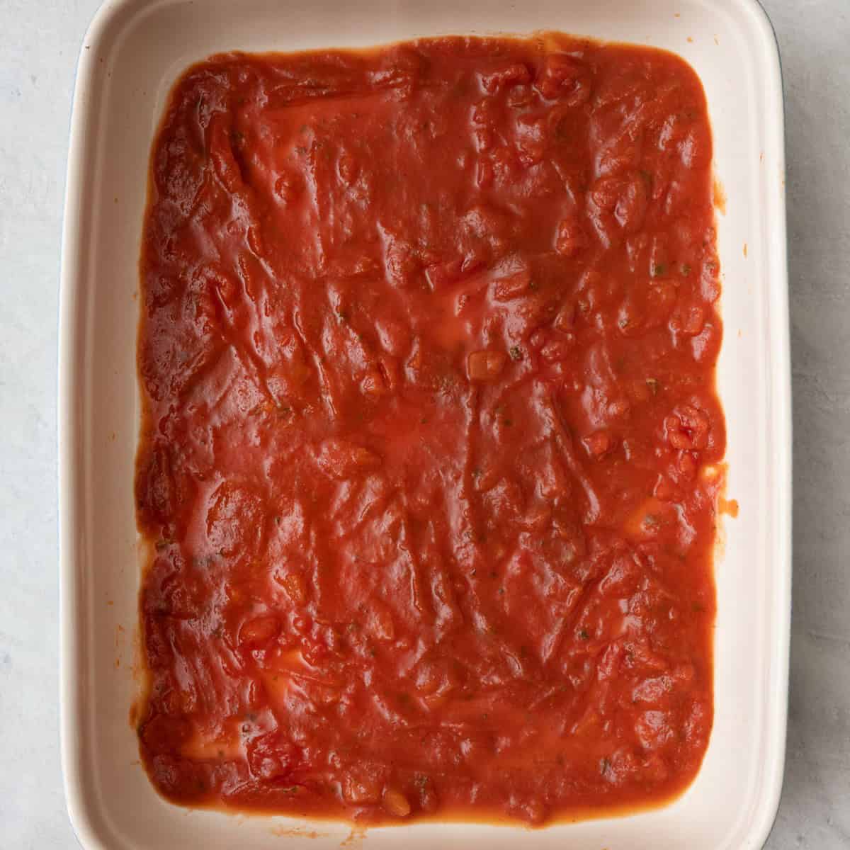 Marinara added to bottom of 9x13 baking dish in an even layer.