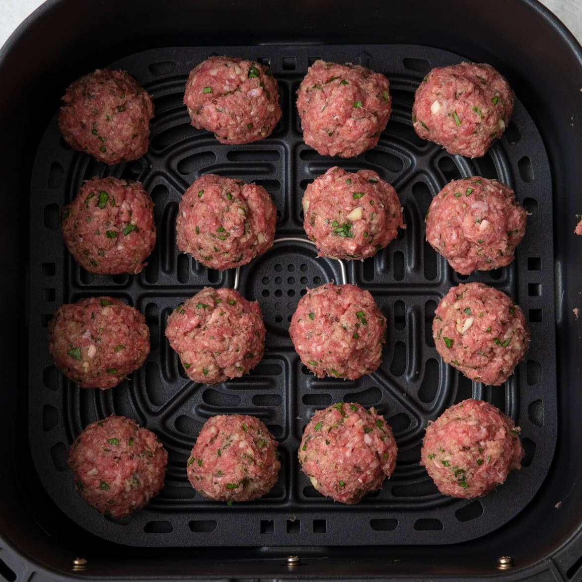 Meatballs in a single layer in air fryer basket before cooked.