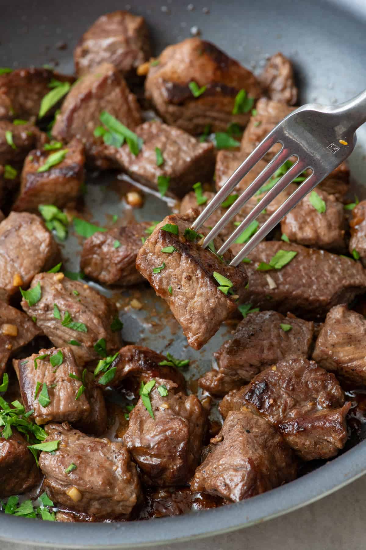 Fork picking up a steak bite from pan garnished with fresh herbs.