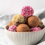 Homemade chocolate truffles decorated three different ways stacked in a bowl with a few next to it.