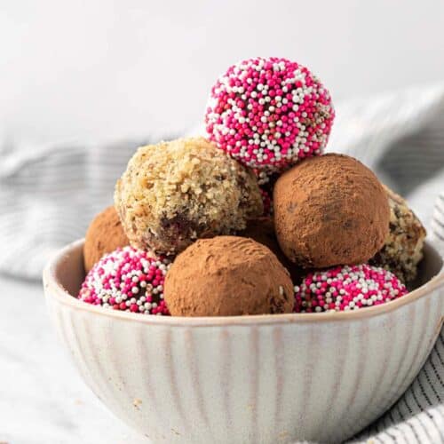 Homemade chocolate truffles decorated three different ways stacked in a bowl with a few next to it.