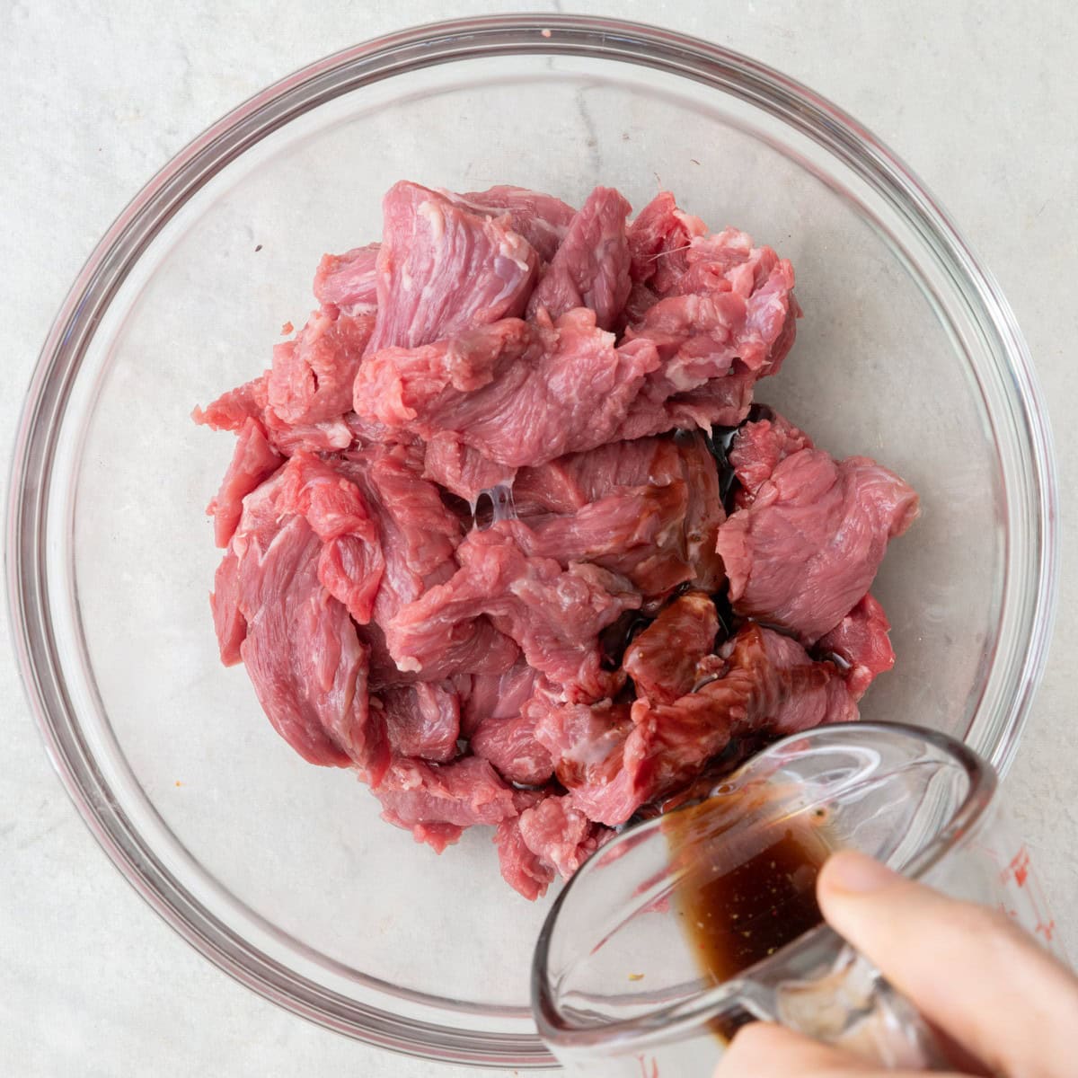 Pouring marinade over beef in bowl.