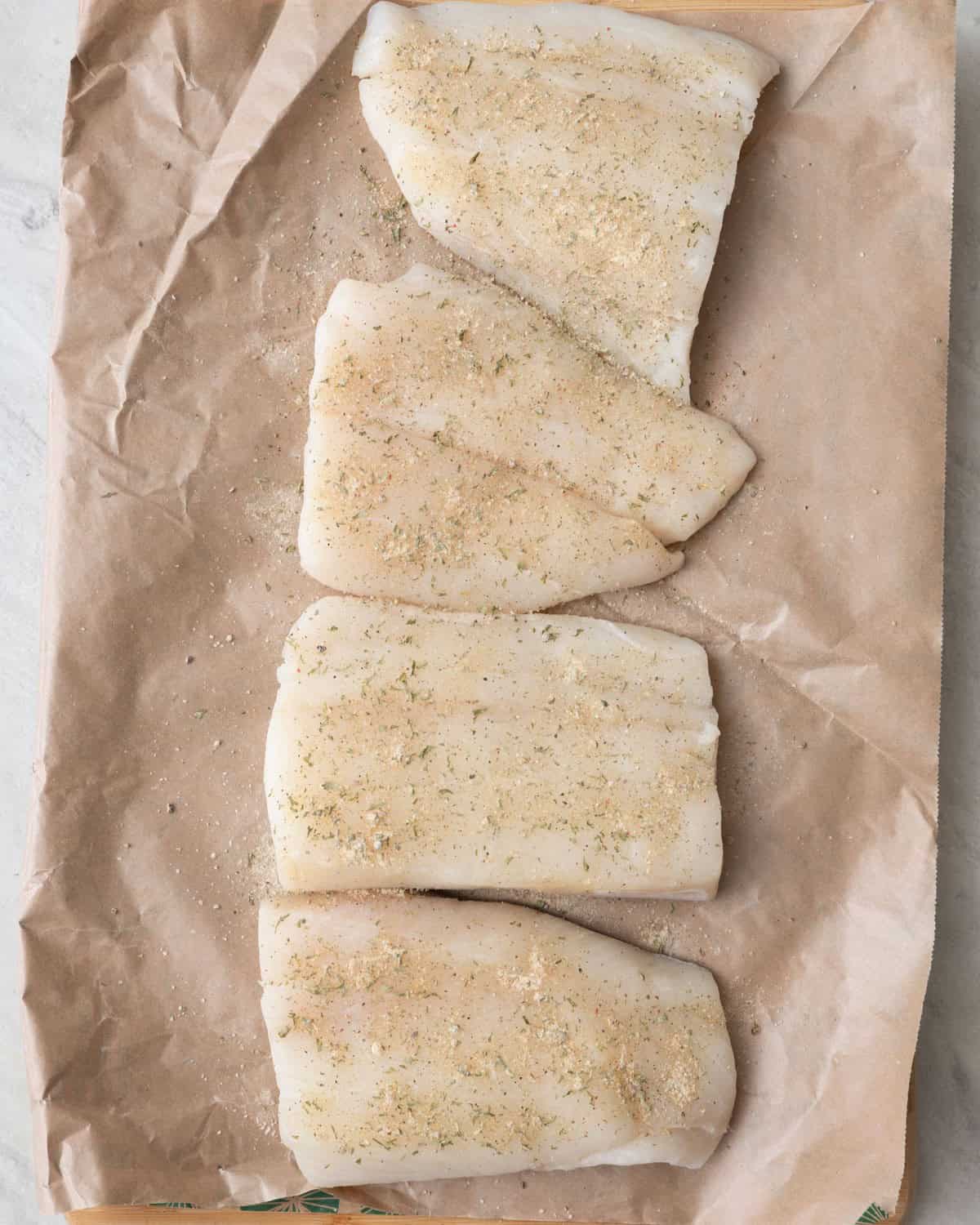 Season halibut on plate, cutting board, or fish wrapping paper it comes in.