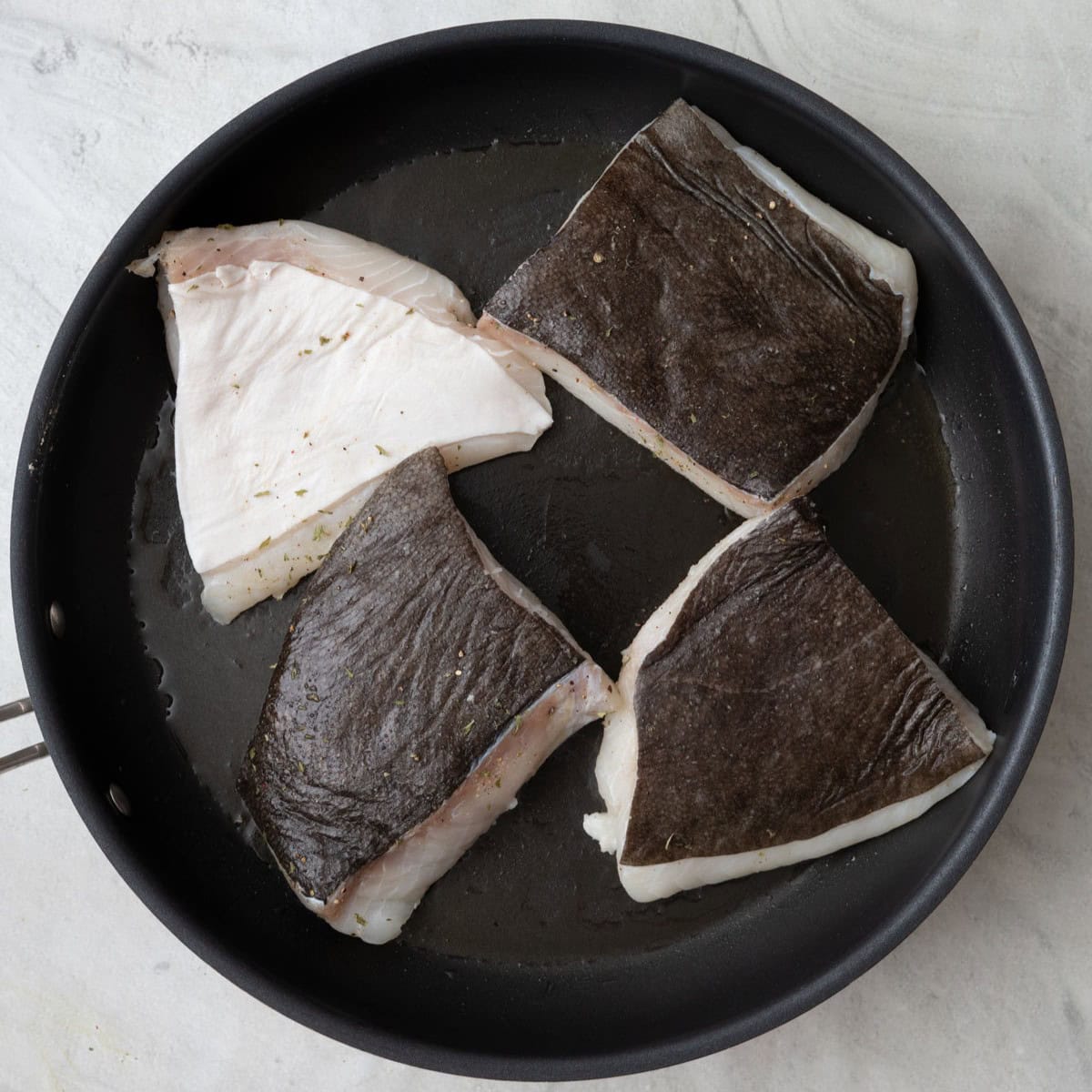 Seasoned halibut skin side up in skillet with oil.