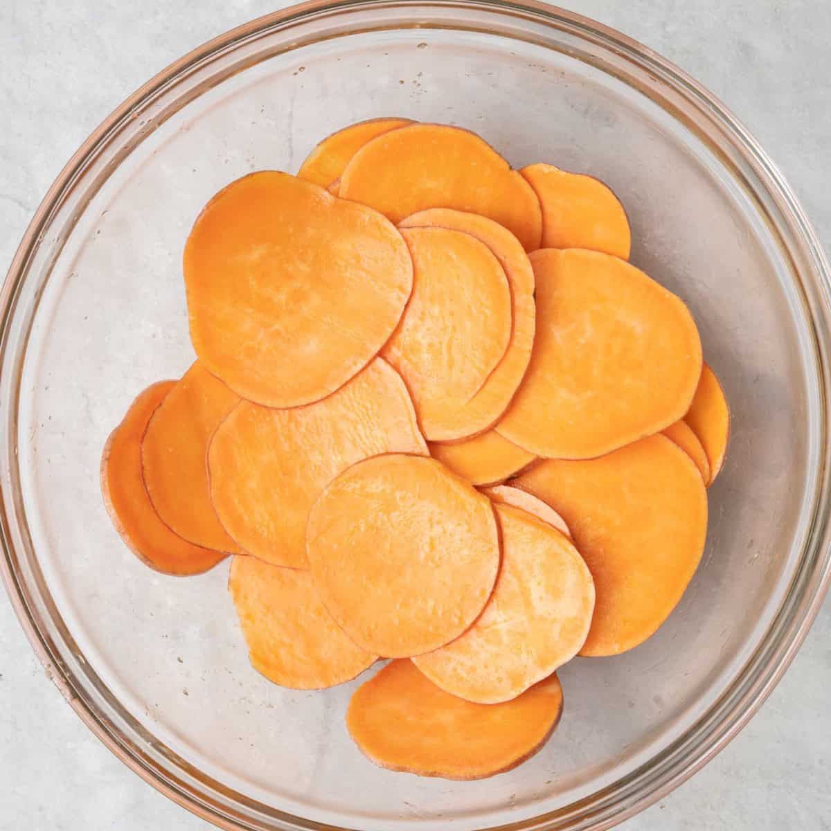 Sweet potato slices in bowl tossed with oil and salt.