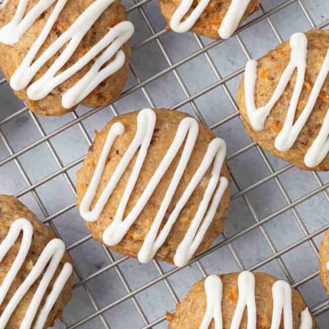 Close up of carrot cake cookies on a wire rack with a zig zag drizzle of icing on top of each cookie.