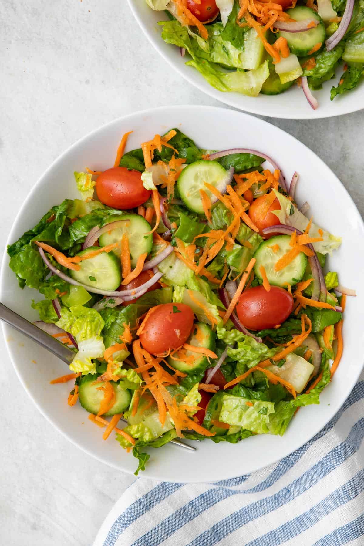 Fully tossed garden salad in a serving bowl with cherry tomatoes, sliced cucumbers, red onions, and shredded carrots.