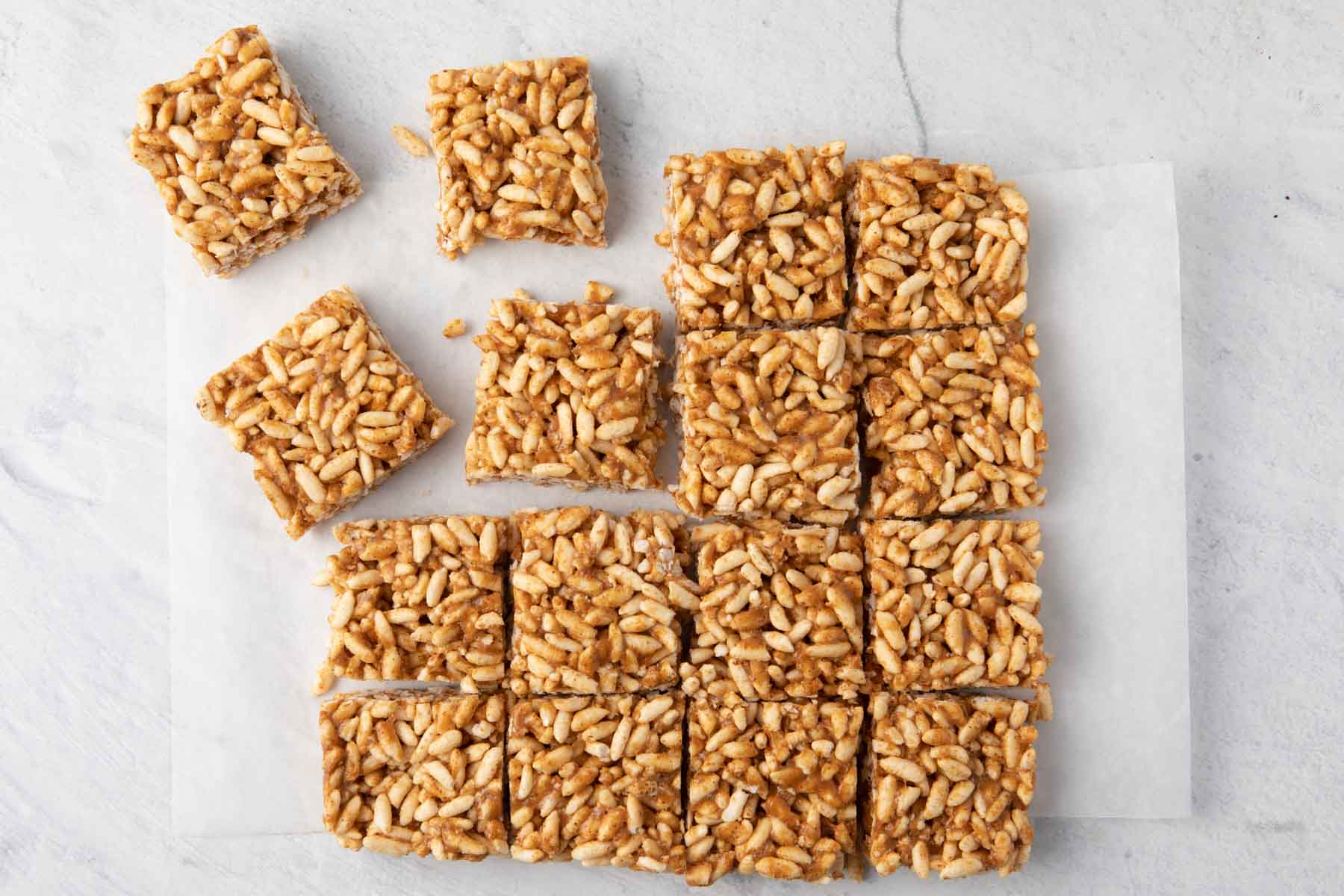 Whole rice krispy treats out of the pan but still on parchment paper cut into 16 even squares with some pulled away.