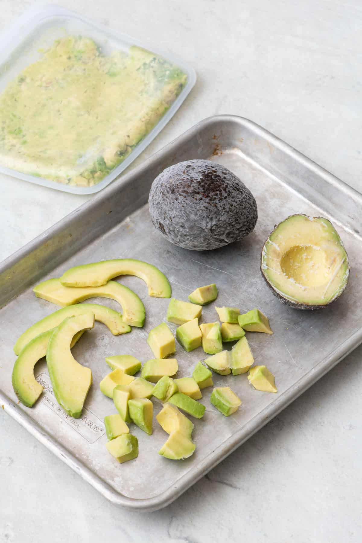 Frozen avocados prepared different ways: mashed in a bag, whole, halved, sliced, and diced on a small baking sheet.