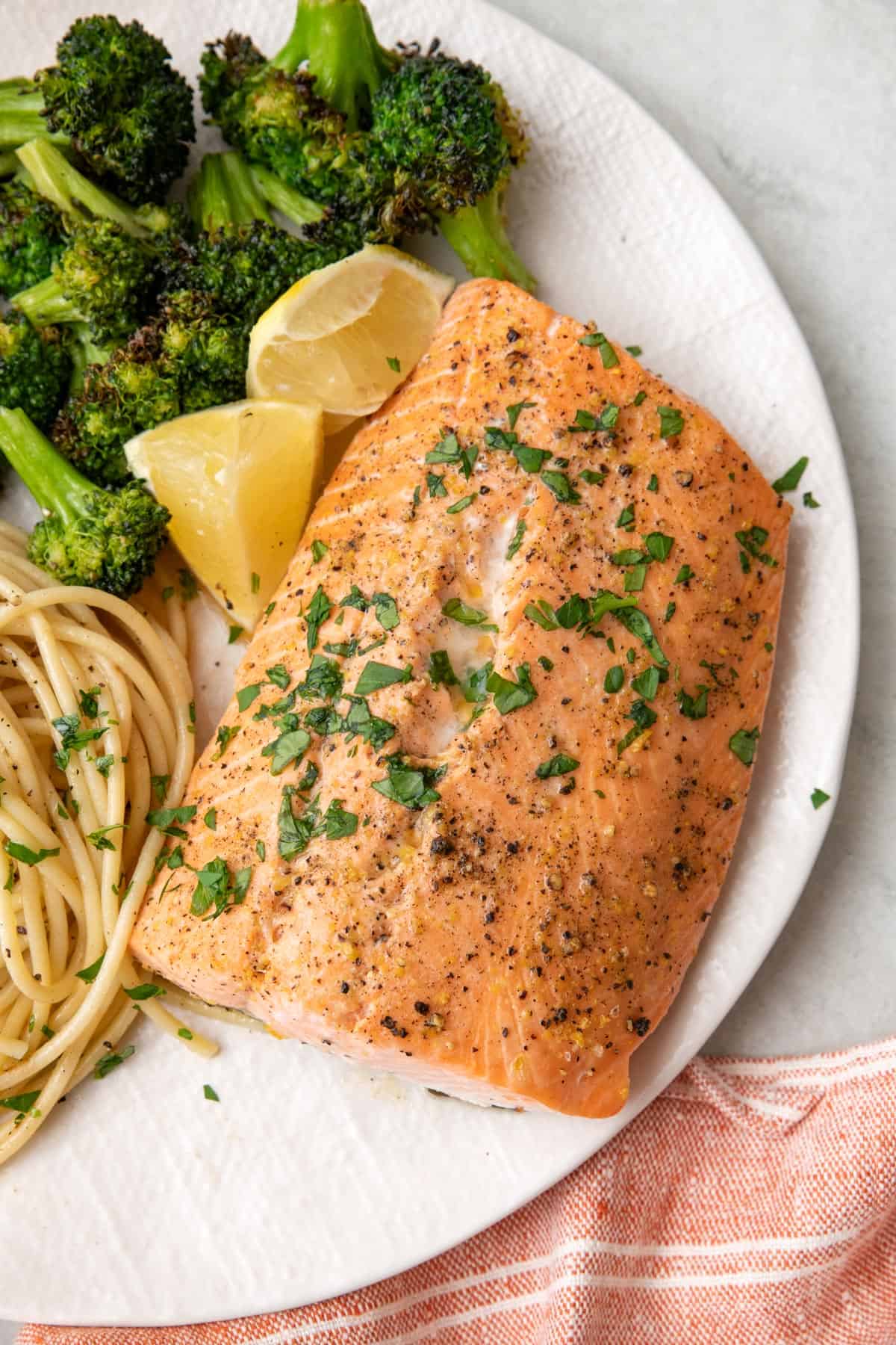Lemon pepper salmon on plate with broccoli and pasta, garnished with fresh parsley and lemon wedges.