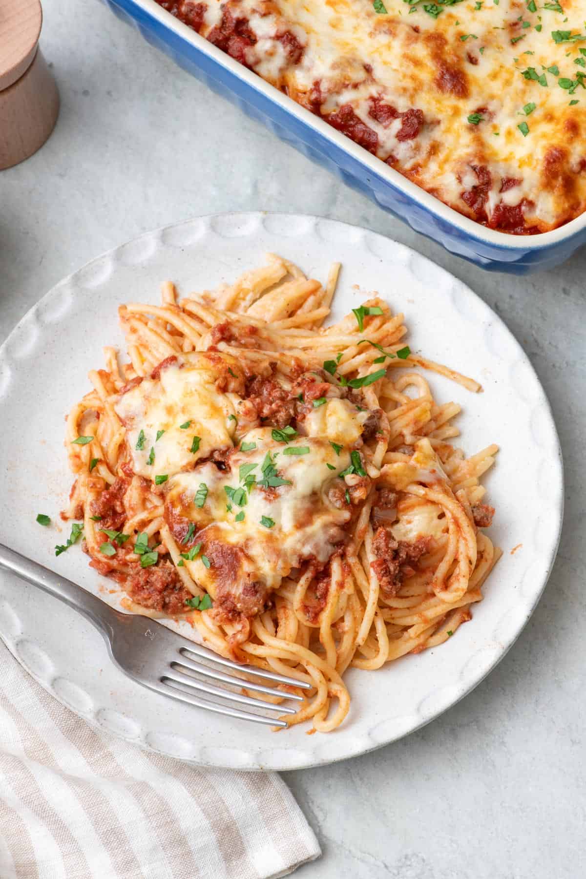 Serving of macarona bechamel on a plate with fork on side and baking dish nearby.