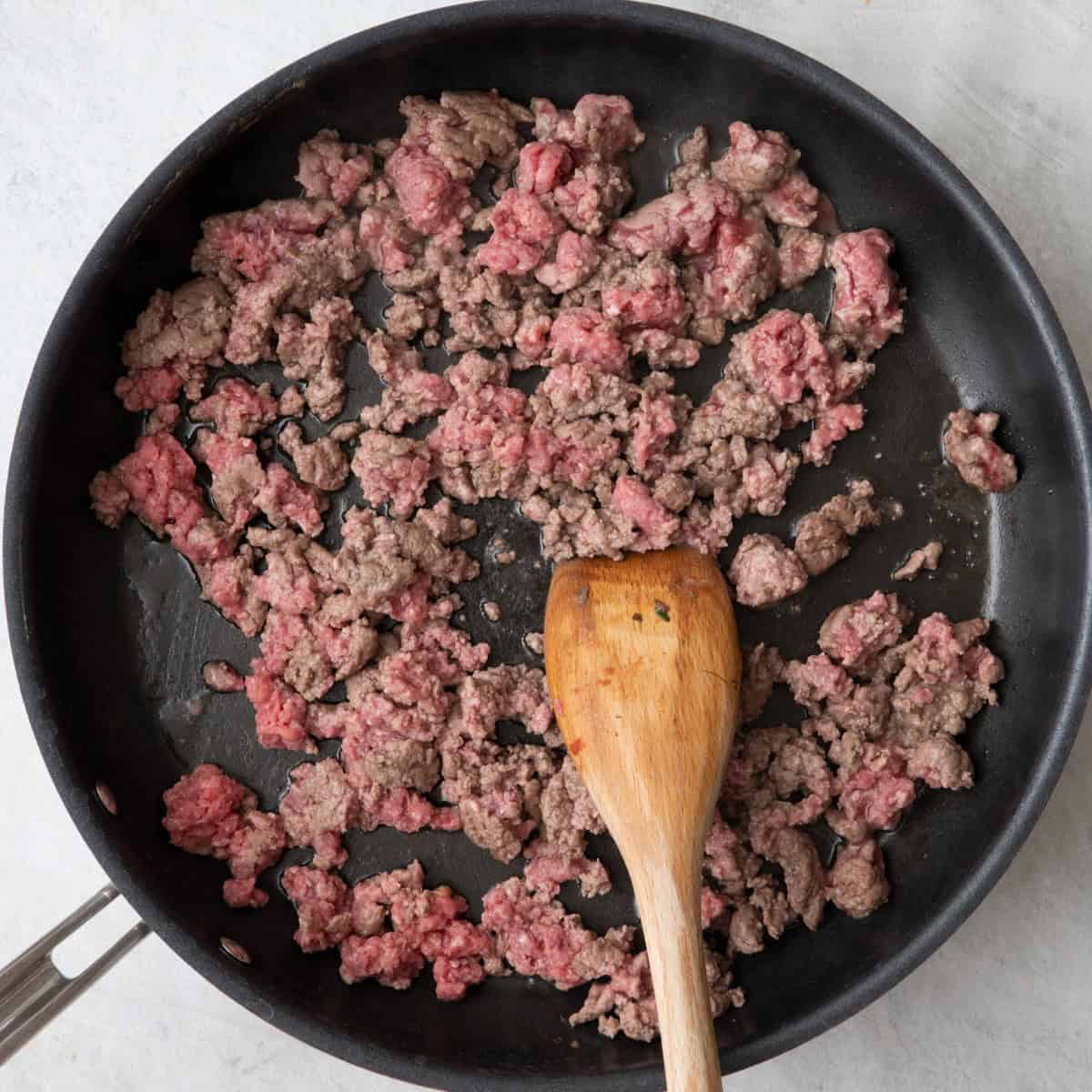 Breaking up ground beef in skillet with wooden spoon or spatula.