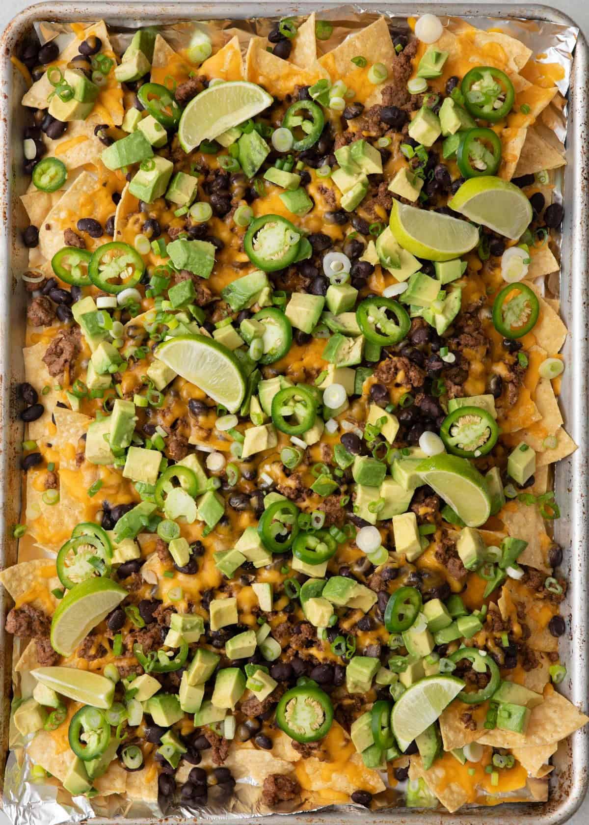 Nachos topped with scallions, jalapenos, avocado, and lime wedges.