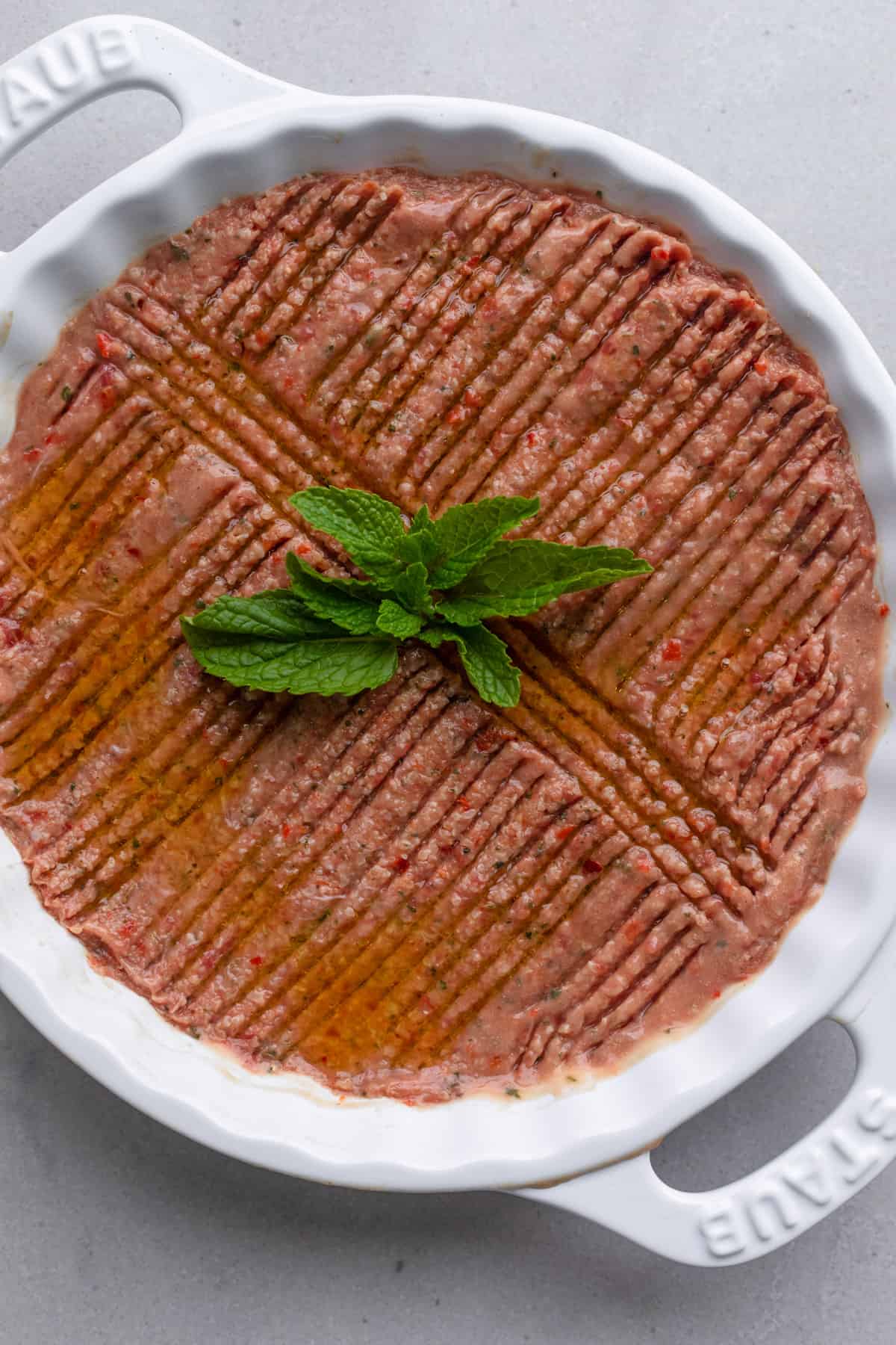 Round ceramic dish with Kebbeh Nayyeh pressed inside with decorative groves pressed into the raw beef mixture.