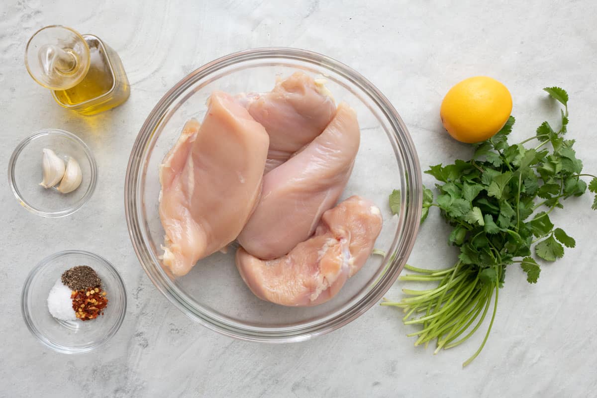 Ingredients for recipe: oil, garlic cloves, spices, chicken breasts, lemon, and cilantro.
